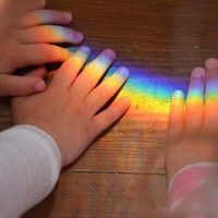 Photo of children's hands with rainbow light shining on them.