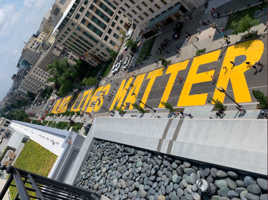 Words painted in bold yellow run the length of several blocks of a street and read "black lives matter"